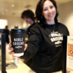A women handing over a cup of Noble Ground Coffee